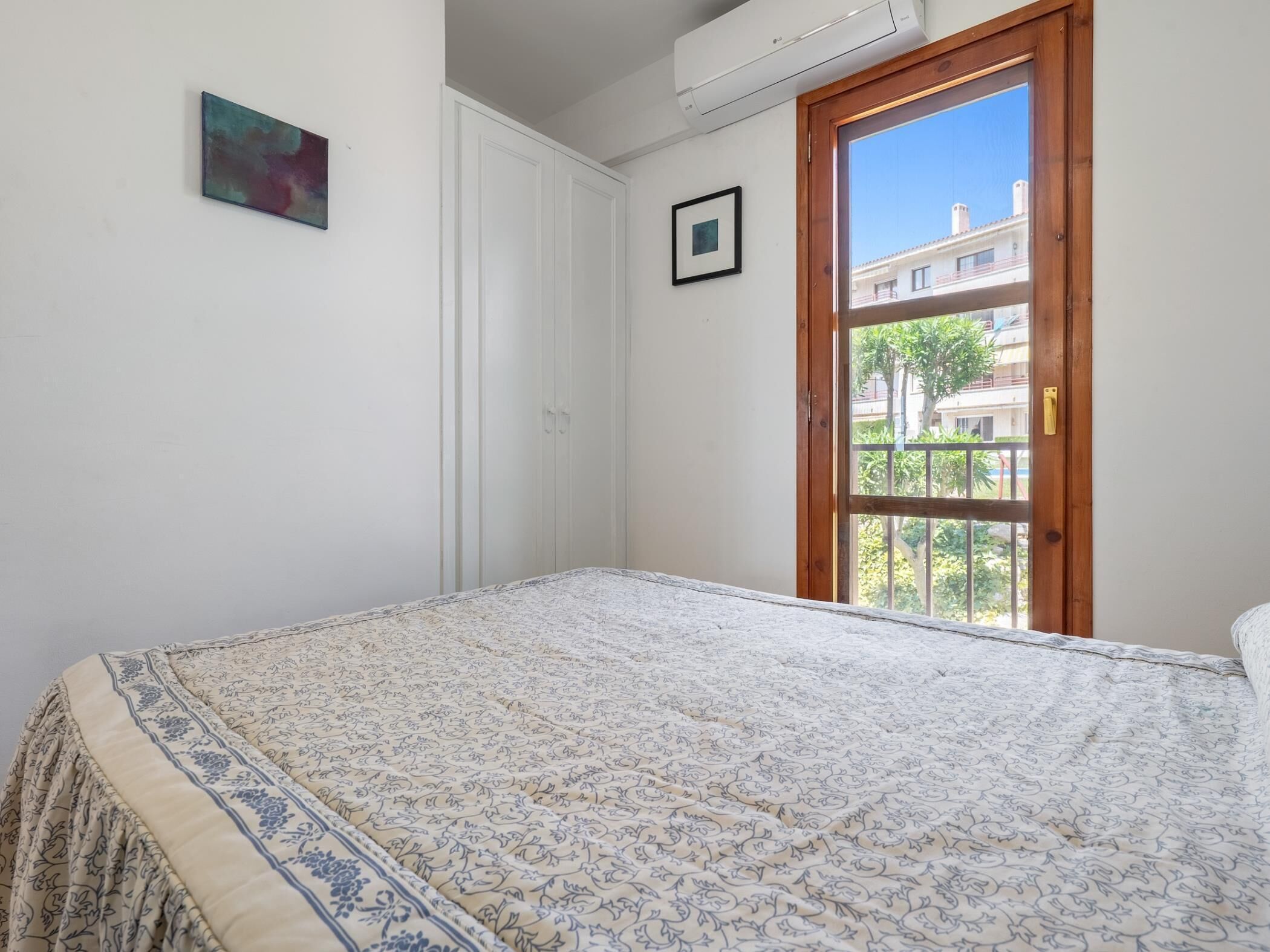 A bedroom with a bed, a door to an outdoor balcony, and a small framed picture on the wall.