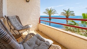 Un balcon doté de meubles en osier, d’une rambarde rouge et offrant une vue sur la mer.