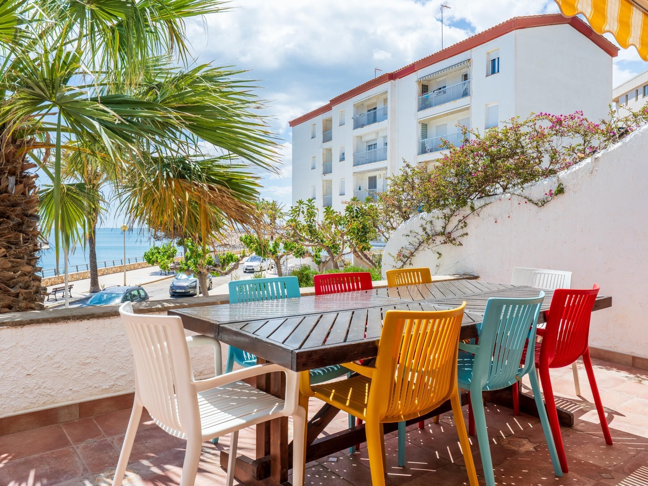 Une terrasse avec une table et des chaises, donnant sur une plage et un immeuble.