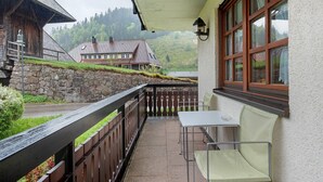 A balcony with a table and chairs, a stone wall, and a view of a house and forest. - Apartment 'Am Blaubeerhang' with Mountain View, Private Terrace and Wi-Fi (Sankt Blasien)