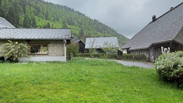 Ein ländliches Dorf mit Steinhäusern, einer grünen Vordergrundfläche und einem bewaldeten Hügel im Hintergrund.