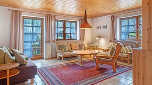 A cozy living room with wooden furniture, a large window with curtains, and a patterned rug. - Apartment 'Am Blaubeerhang' with Mountain View, Private Terrace and Wi-Fi (Sankt Blasien)