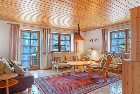 Un salon chaleureux, avec des meubles en bois, une grande fenêtre agrémentée de rideaux et un tapis à motifs.