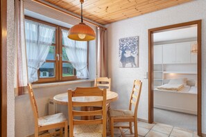 Une pièce comprenant une table ronde en bois, quatre chaises, une fenêtre avec des rideaux, un ventilateur de plafond et un lit avec une tête de lit.