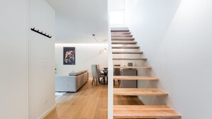 Een modern interieur met een houten trap, een bank, een eettafel en een poster aan de muur.