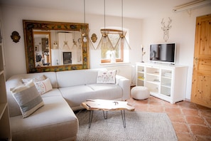 A living room with a sofa, a coffee table, a television on a cabinet, a large mirror, and a wooden door. - Apartment 'Gemütliche Wohnung' with Mountain View, Shared Terrace and Wi-Fi (Anger)