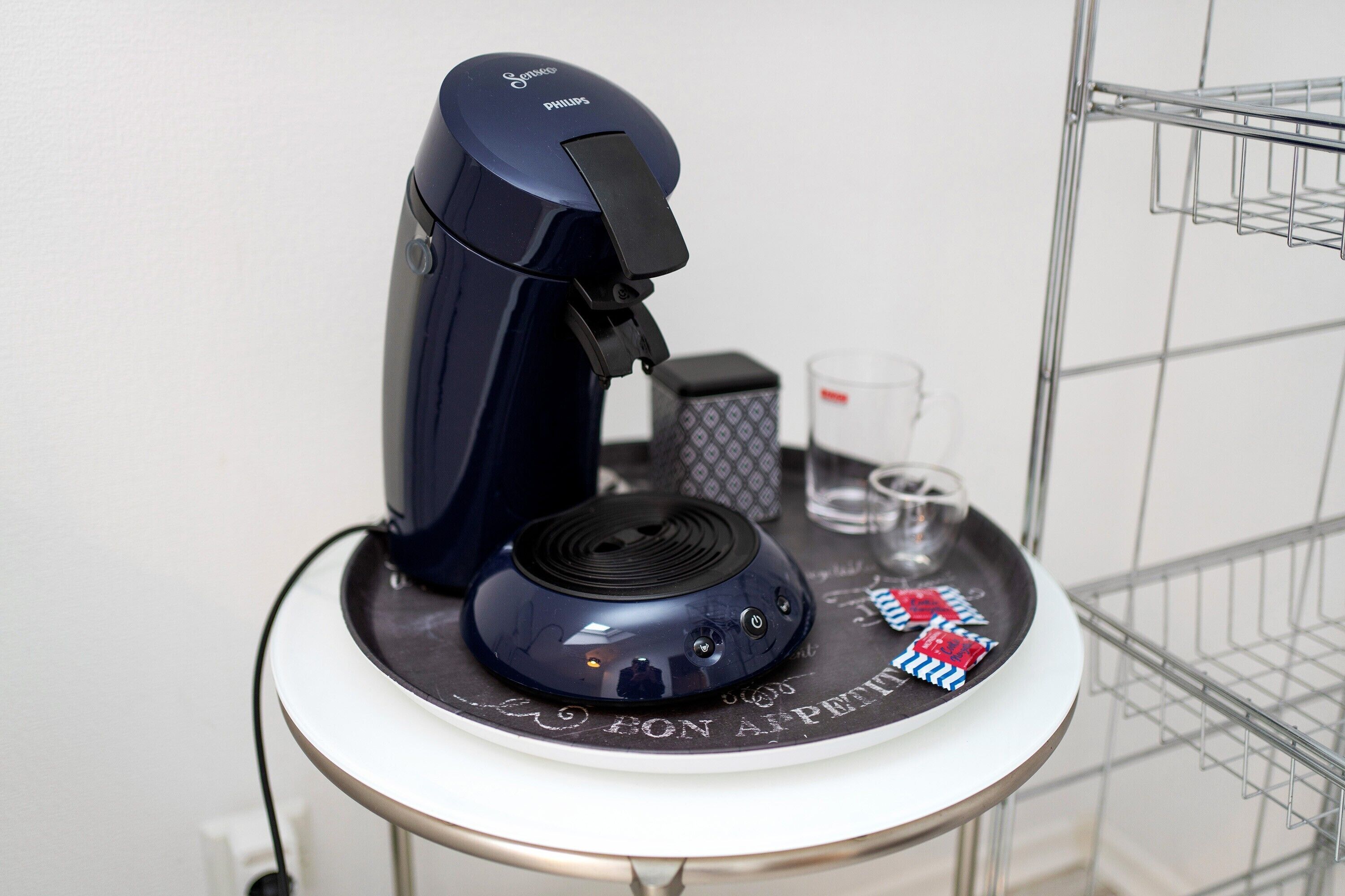 Eine Kaffeemaschine auf einem Tisch mit Tablett, Glas und Taschentuchbox.
