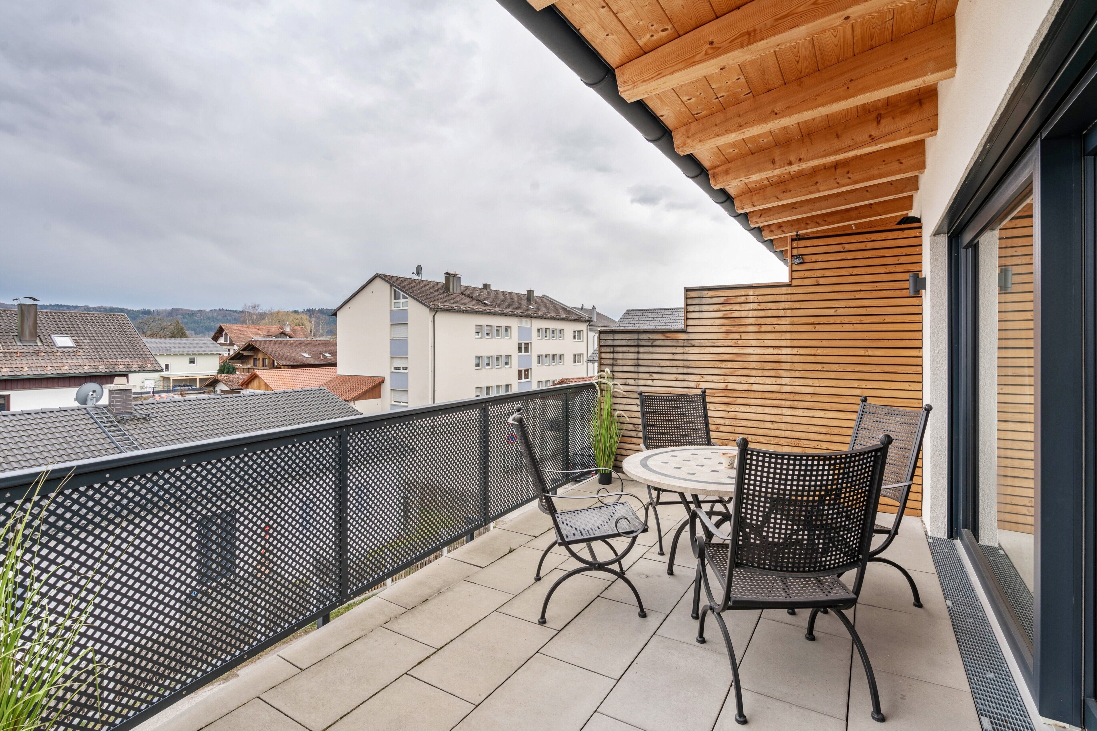 A balcony with a wooden ceiling, a round table with chairs, and a view of buildings in the background.