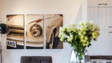 A wall with three framed photographs of a vintage car, a black floor lamp, and a vase with flowers.