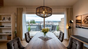 Un espace repas comprenant une table en bois, des chaises, un luminaire suspendu et une vue sur l’extérieur.