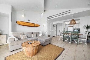 Ein modernes Wohnzimmer mit grauem Sofa, einem Holztisch und einem an der Wand befestigten Surfbrett.