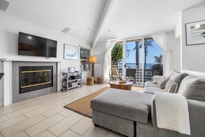 A modern living room with a fireplace, a flat-screen TV, and a view of the sea through large windows.
