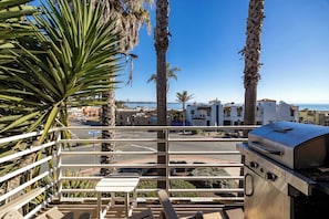 Un balcón con una parrilla, palmeras y vista a la playa y edificios.