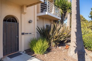 A building with a gated entrance, a balcony, and a small garden with plants and a palm tree.