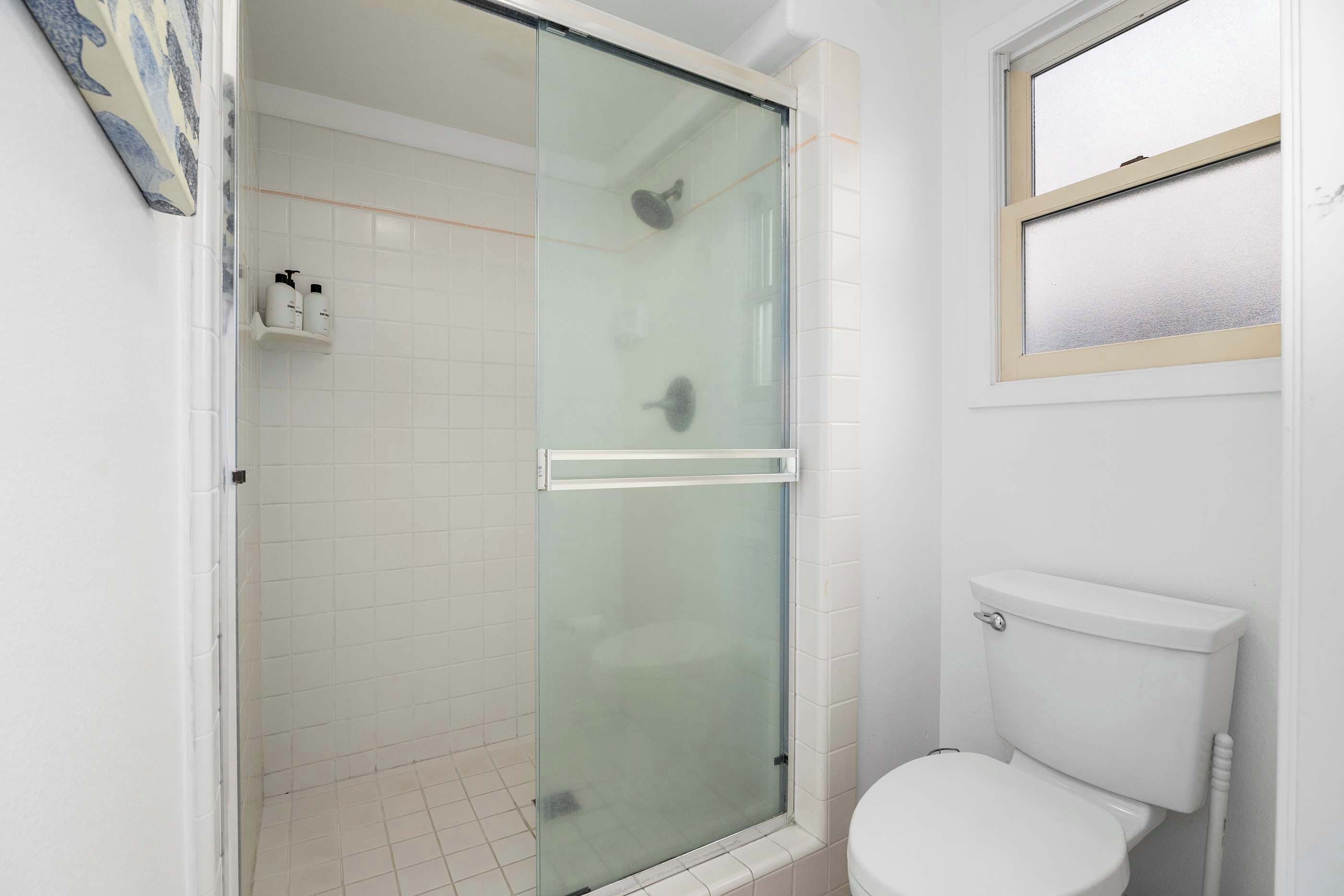 Un baño con cabina de ducha de vidrio, inodoro y ventana.