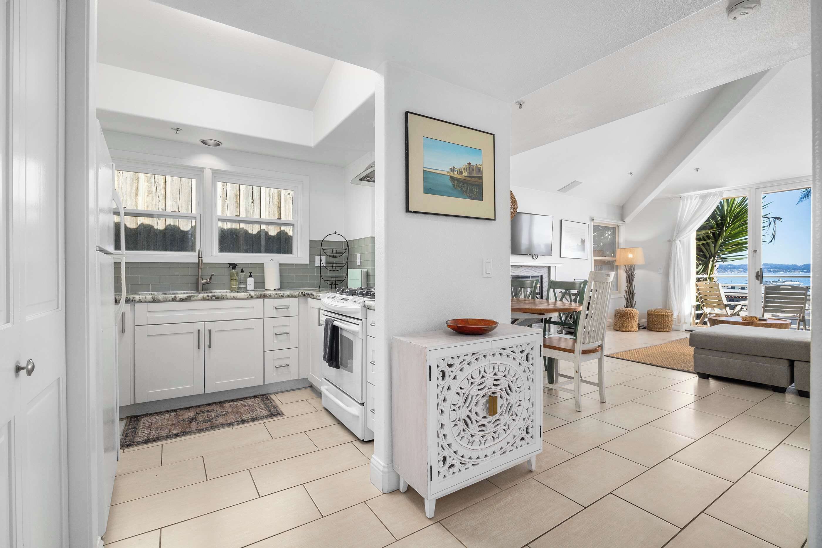 A modern kitchen with white cabinetry, a built-in oven, and a dining area with a table and chairs.