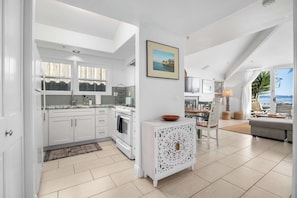 A modern kitchen with white cabinetry, a built-in oven, and a dining area with a table and chairs. - Capitola Village Condo - 1 min walk to beach (Capitola)