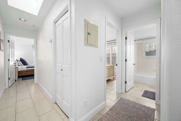 A hallway with white walls, a bed, a bathroom with a bathtub, and a shower.