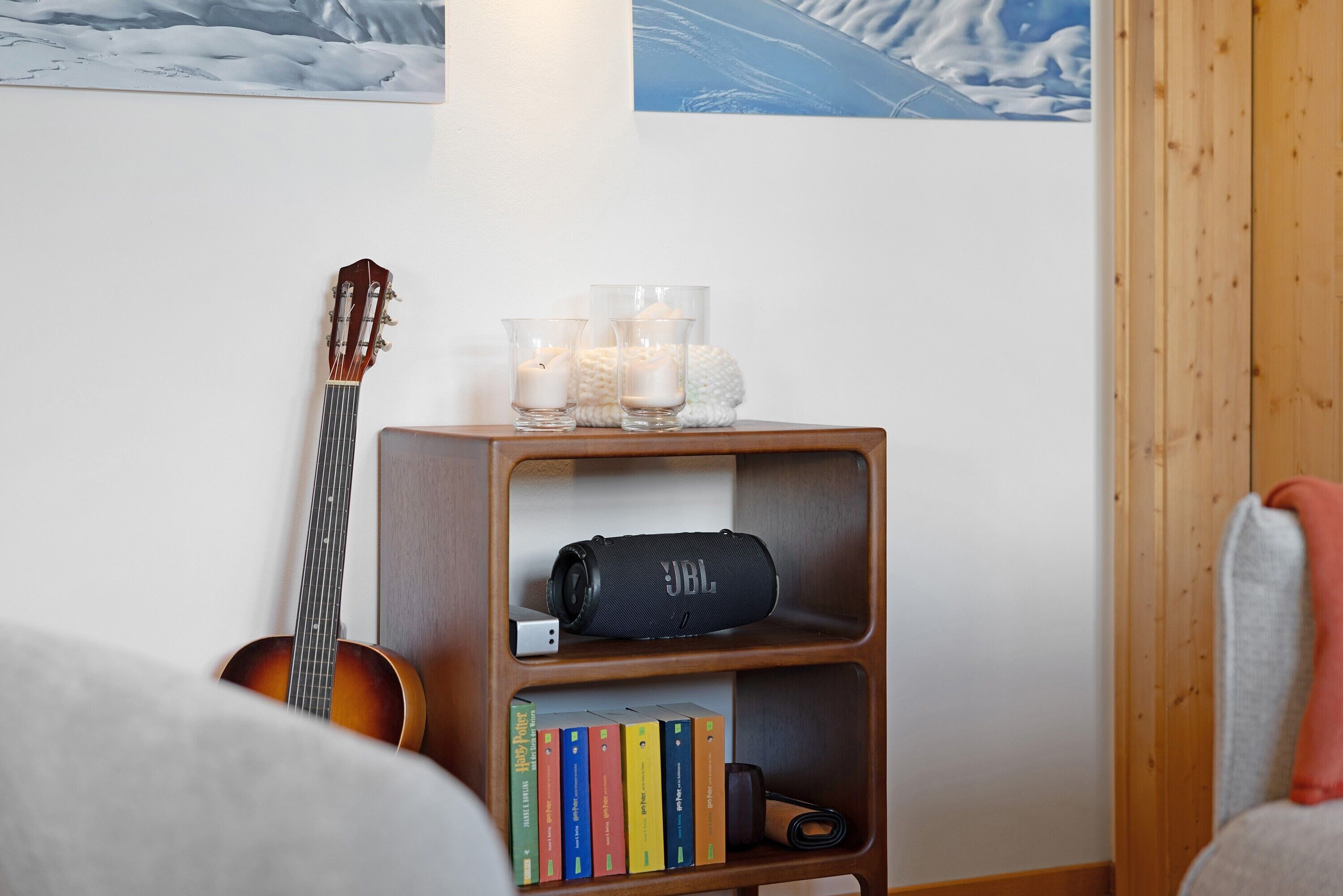 En bokhylla i trä med en gitarr, böcker, ljus och en högtalare från JBL.