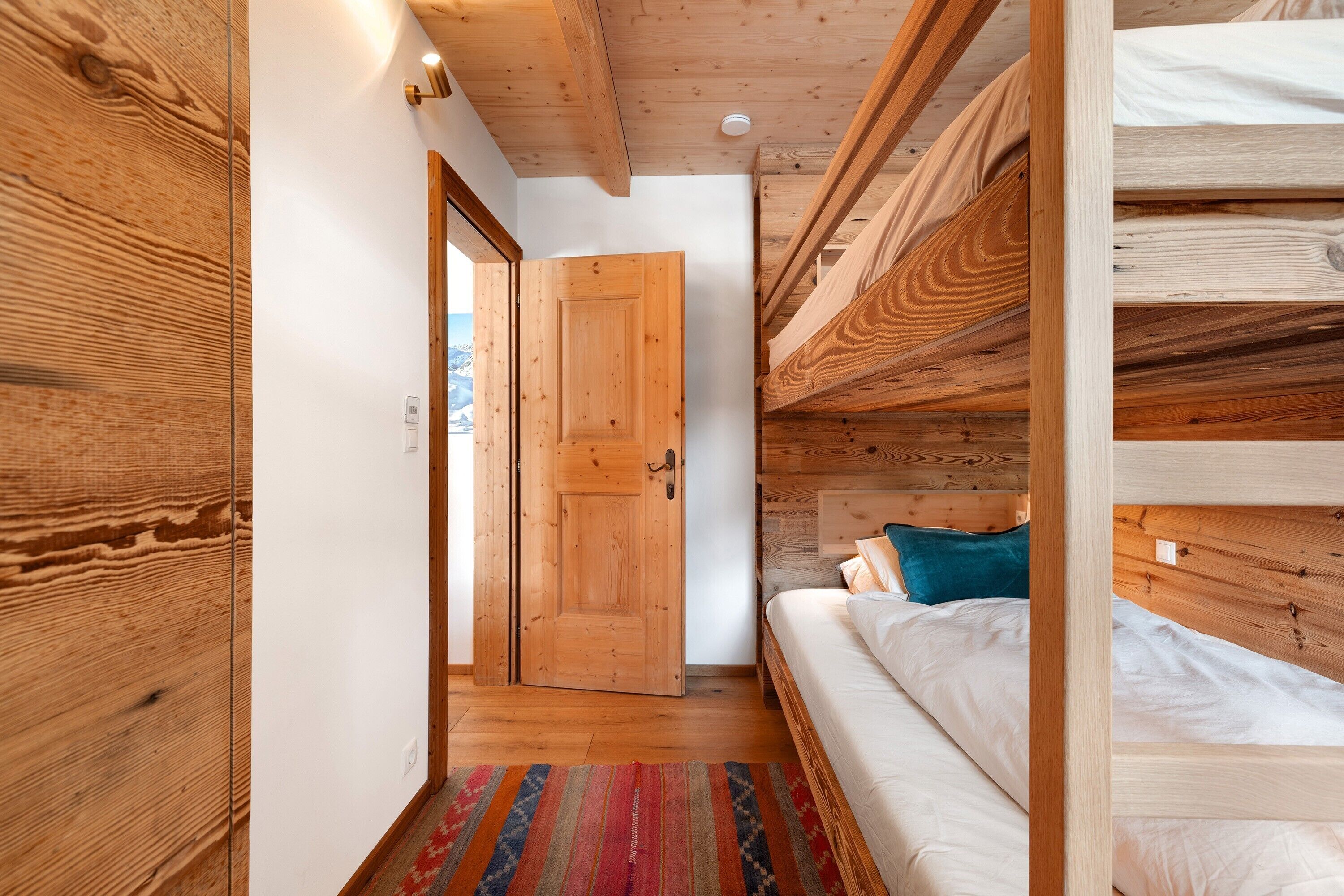 Interior de madera con una litera, una puerta y una alfombra estampada.