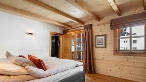 A wooden-paneled room with a bed, a window with curtains, and a door leading outside. - Holiday Appartment "Steinbock" in Sankt Anton am Arlberg with Mountain View, Balcony and Wi-Fi (Sankt Anton am Arlberg)