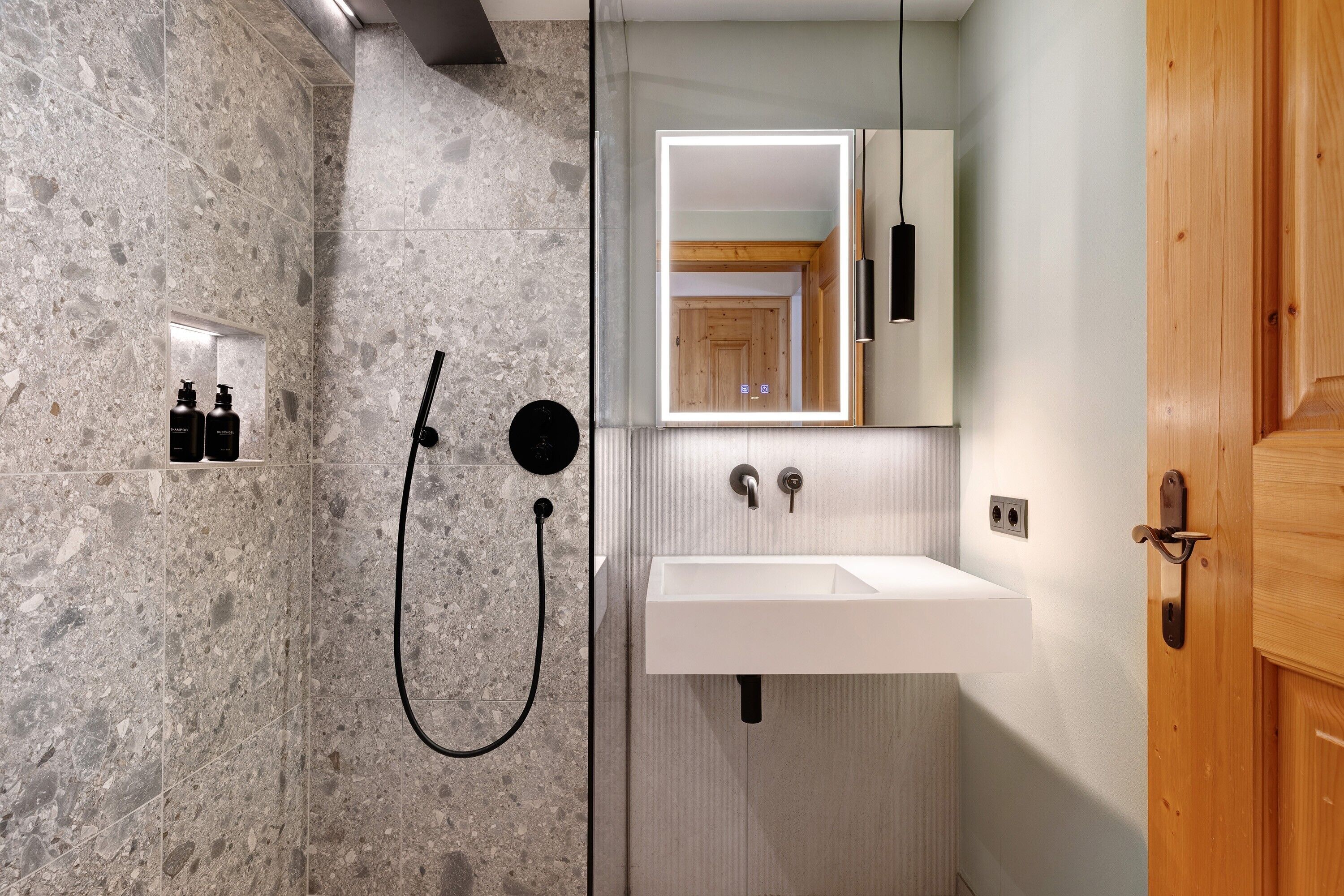 A bathroom with a marble wall, a sink, a mirror, and a wooden door.