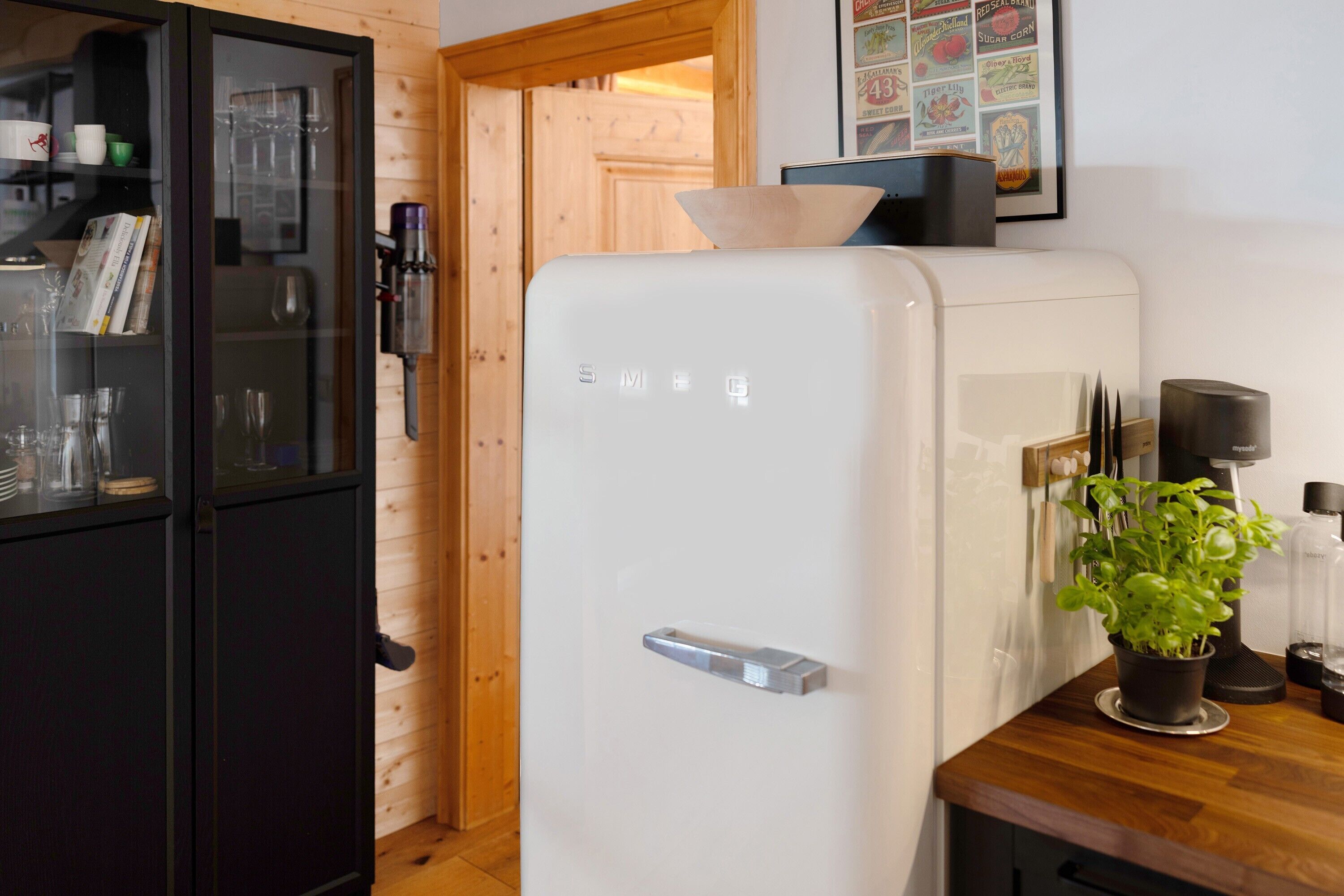 Keittiössä on valkoinen jääkaappi, mustat lasiovet, puinen ovi ja ruukkukasvi työtasolla.