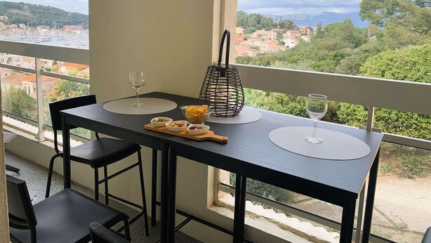 A balcony with a table set for two, a wine glass, and a basket of snacks. - Nice 1 bedroom apartment, WIFI, sea view, all on foot (ST MANDRIER SUR MER)