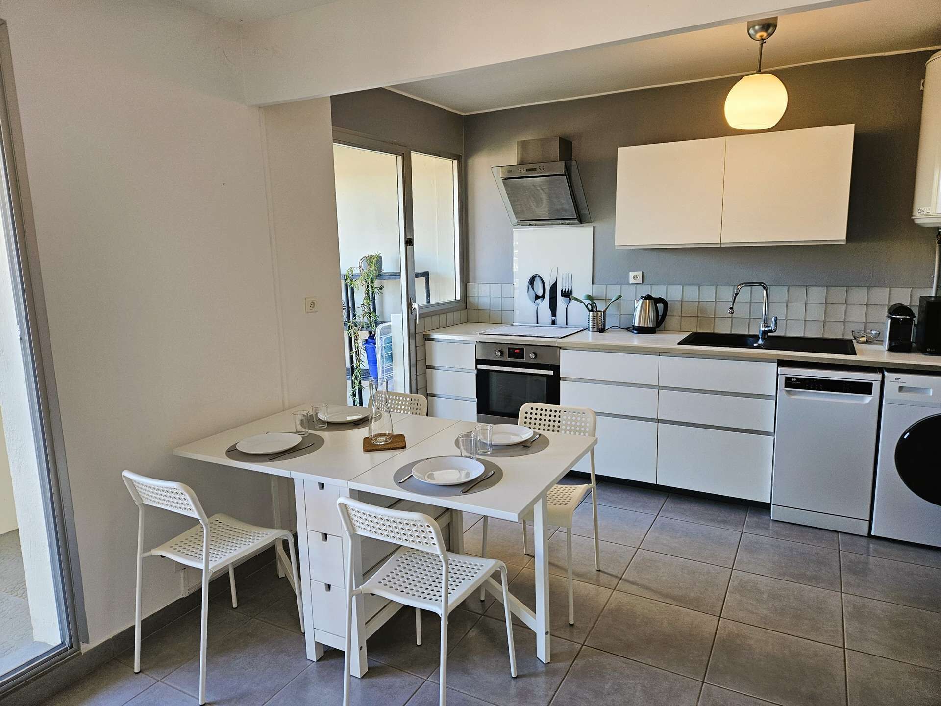 Une cuisine moderne avec des meubles blancs, une table à manger avec des chaises et une fenêtre qui laisse entrer la lumière naturelle.