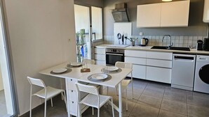 A modern kitchen with white cabinetry, a dining table with chairs, and a window providing natural light. - Nice 1 bedroom apartment, WIFI, sea view, all on foot (ST MANDRIER SUR MER)