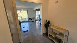 A hallway leading to a dining area with a table and chairs, a potted plant, and a shelf with a vase. - Nice 1 bedroom apartment, WIFI, sea view, all on foot (ST MANDRIER SUR MER)