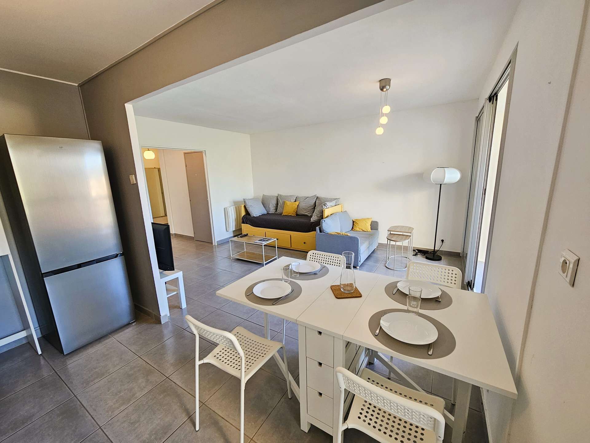 A modern kitchen with a dining area, a refrigerator, and a sofa in the background.