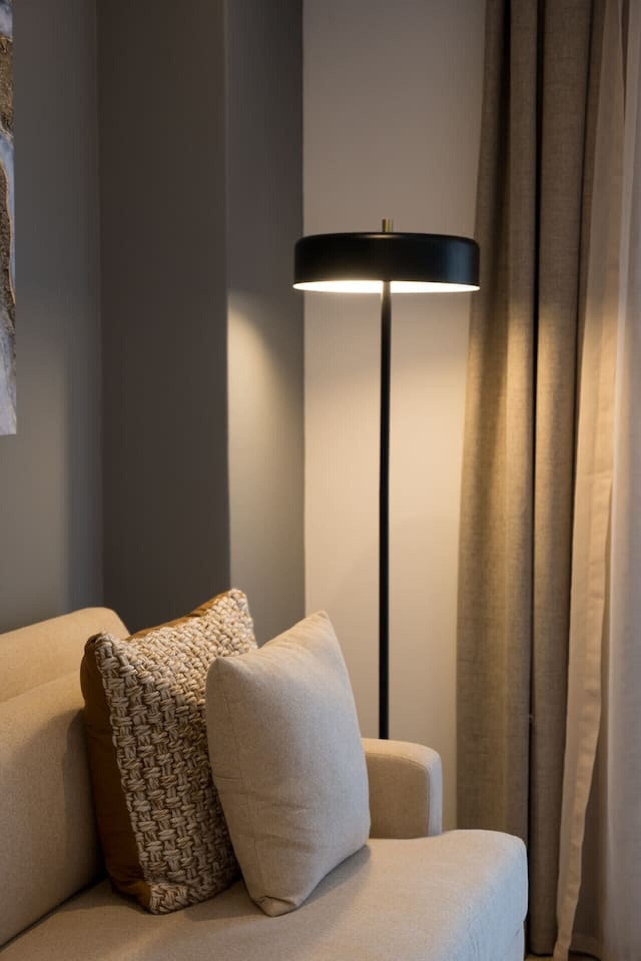 A corner of a room with a sofa, a floor lamp, and curtains.