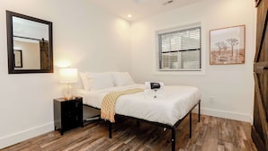 A bedroom with a bed, bedside table, lamp, and artwork on the wall. - Sojourn 2 BR Steps to the Beach Sleeps 4 (Virginia Beach)