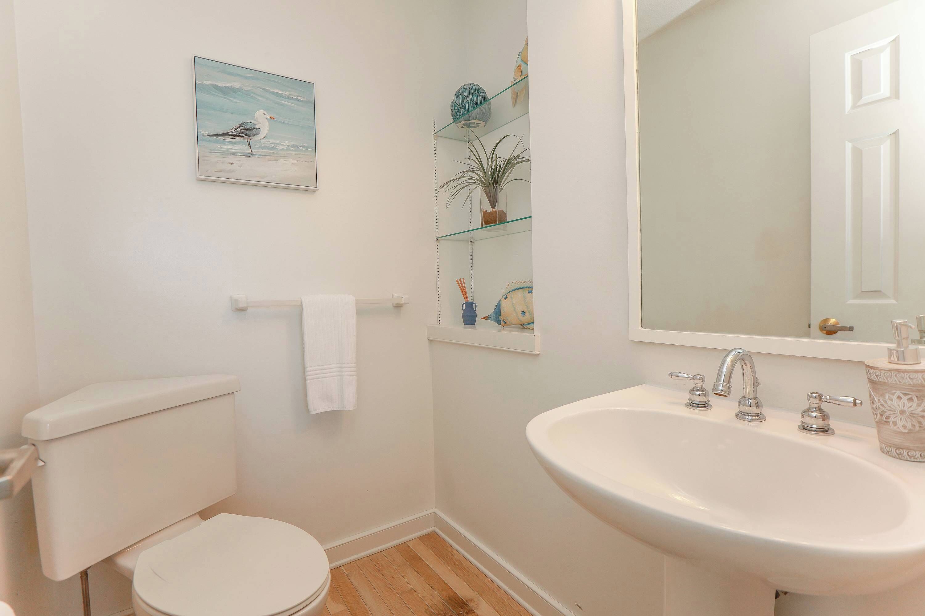 A bathroom with a toilet, sink, mirror, and a shelf with a potted plant.