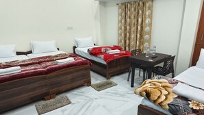 Une chambre d’hôtel avec deux lits, une petite table avec des chaises, une armoire en bois et une fenêtre avec des rideaux.