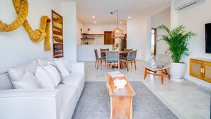 A modern living room with a white sofa, a wooden coffee table, and a dining area with a table and chairs. - Casa Manglar - Golf Course Views, Near the Ocean (Puerto Aventuras)