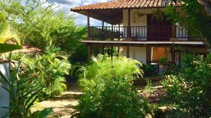 A two-story house with a tiled roof, surrounded by lush greenery and a garden. - Spacious Family Room – Achiotte, Colombia (Barichara)