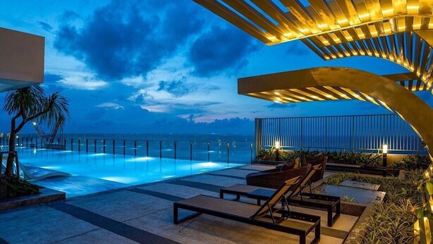 Ein Poolbereich mit Liegestühlen, einer Brüstung und Blick auf den Ozean im Abendrot.