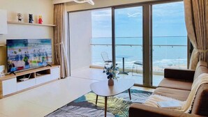 Ein modernes Wohnzimmer mit großem Fernseher, einer Couch, einem Couchtisch und Meerblick durch große Fenster.