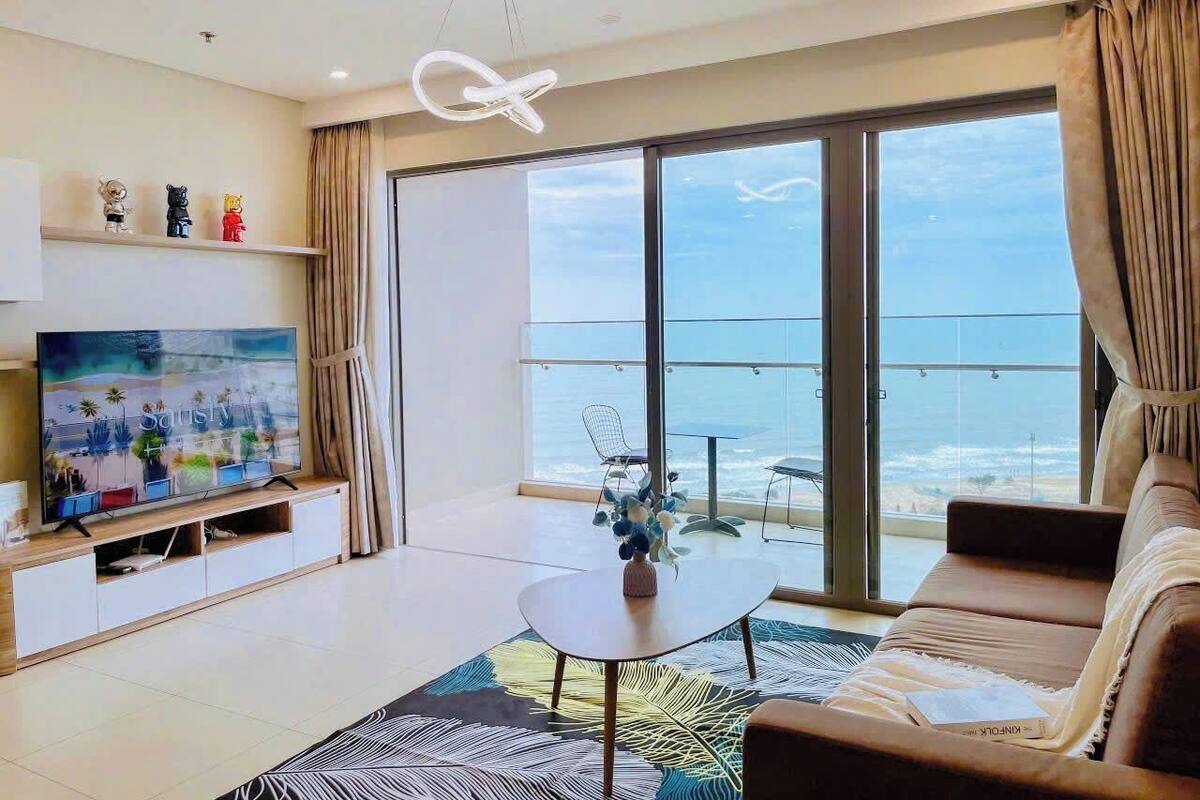 Ein modernes Wohnzimmer mit großem Fernseher, einer Couch, einem Couchtisch und Meerblick durch große Fenster.