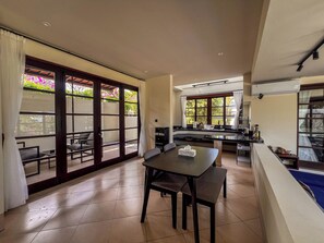 A spacious dining area with a table and chairs, a kitchen area with a sink and countertop, and large sliding glass doors leading to an outdoor patio. - Bumi Ola Villa Pandawa (Kutuh)