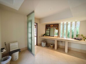 A modern bathroom with a large mirror, a toilet, a trash bin, and a sink. - Bumi Ola Villa Pandawa (Kutuh)