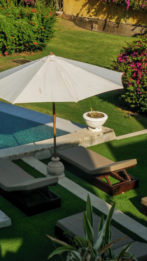 An outdoor pool area with a white umbrella, lounge chairs, and a small planter.