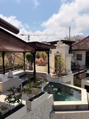 Zona de piscina en la azotea con pérgola, asientos y vista a una obra en construcción de fondo.