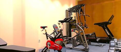 Uma academia com equipamentos de cardio, aparelhos de musculação e um banco.