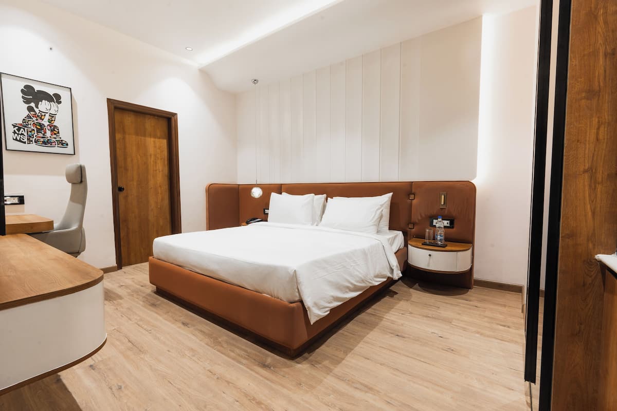 A modern bedroom with a wooden floor, a bed with white bedding, a nightstand, a desk, and a chair.