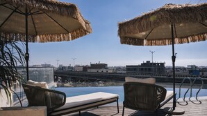 A poolside area with two wicker chairs and thatched umbrellas, overlooking a cityscape and a bridge. - AVA Hotel Chandigarh Zirakpur (Dera Bassi)