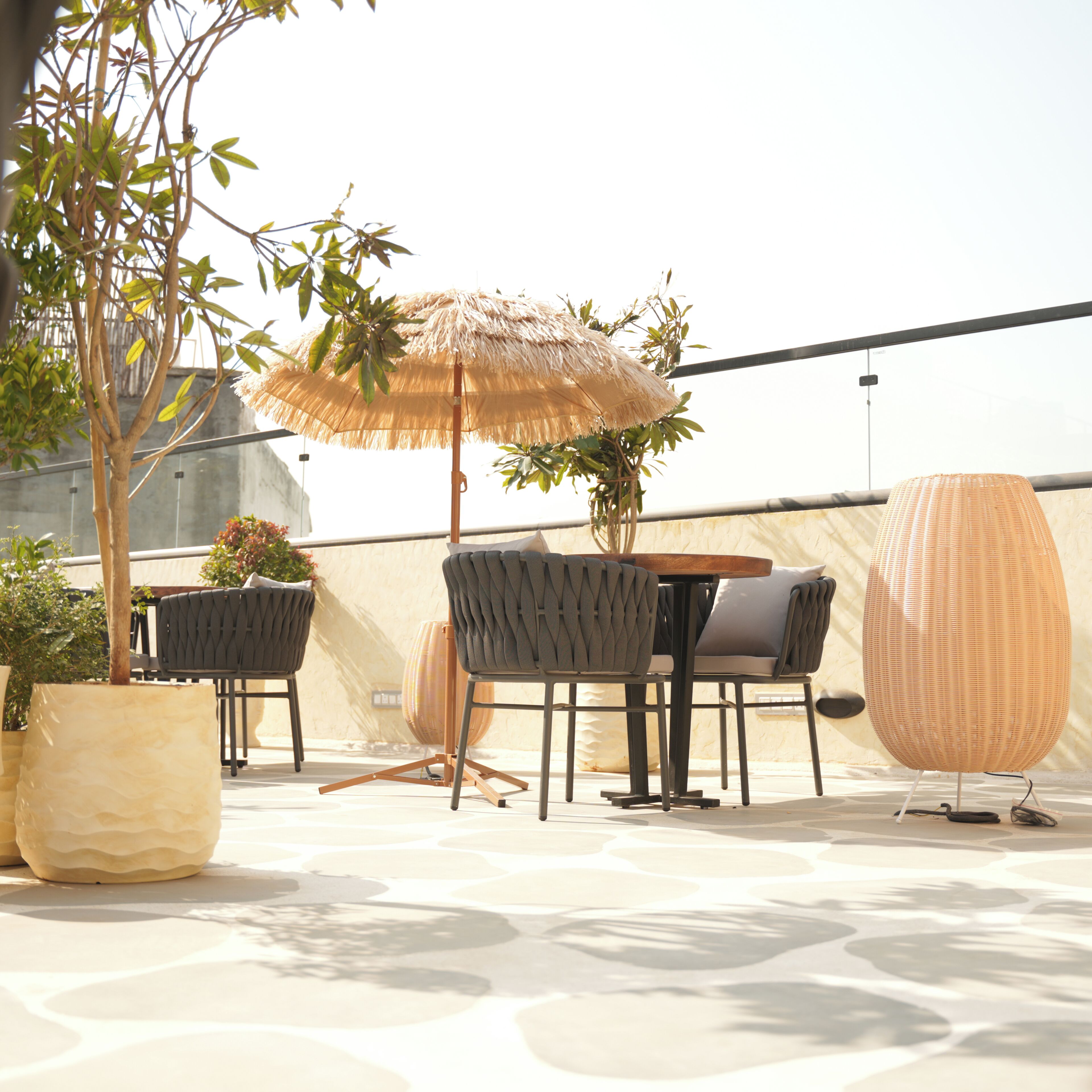 Un espace extérieur aménagé avec une table et des chaises, un parasol en chaume et des plantes en pot.
