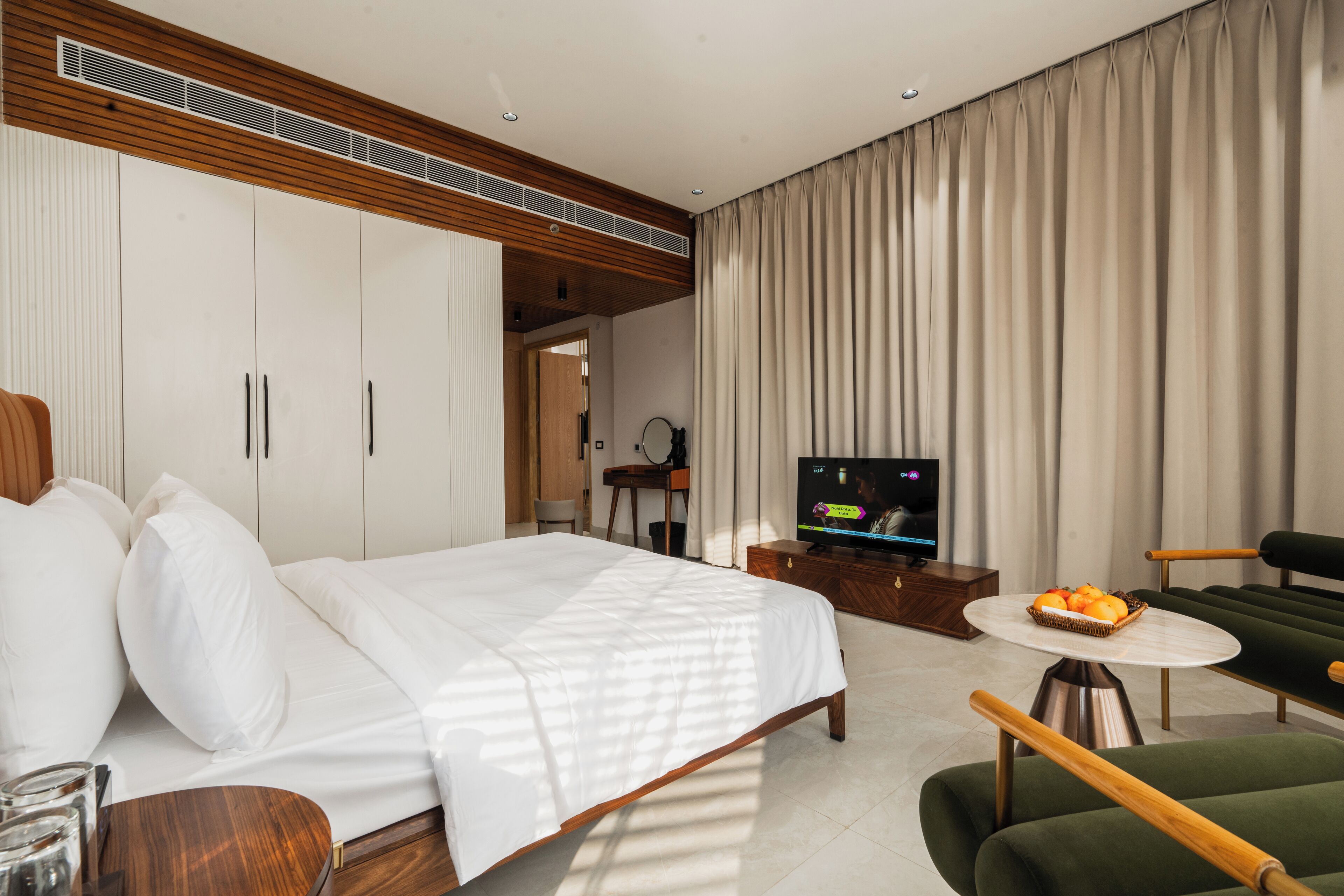 A modern hotel room with a large bed, a TV, a dining table, and a sofa.